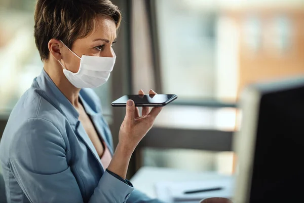 Business woman in a medical protective mask works at the computer and talking on a smartphone during self-isolation and quarantine to avoid infection during flu virus outbreak and coronavirus epidemic