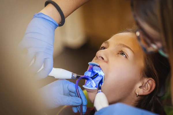 その少女は歯医者にいる 歯医者は赤外線ランプで歯にブレースをつけます — ストック写真