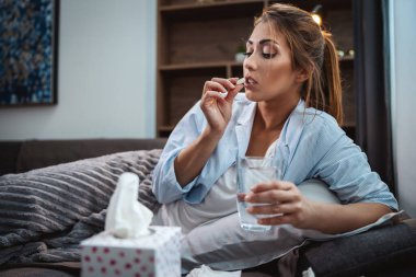 Genç kadın hasta yatarken kanepede ve ilaç alıyor..