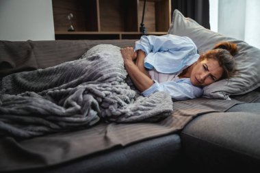 Genç ve çekici bir kadın evdeki kanepesinde hasta yatıyor ve adet sancısı çekiyor..