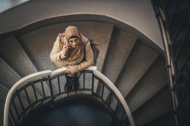 Orta yaşlı, tesettürlü Müslüman iş kadını evinin merdivenlerinde dikiliyor ve akıllı telefonunu alıyor..