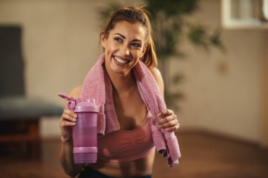 Genç bayan evdeki oturma odasında antrenman yapıyor. Dinleniyor ve sabah güneşinde su içmeye hazır..