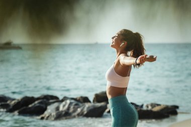 Güzel bir genç kadın yaz güneşli bir günde deniz sahilinde esneme egzersizi yapıyor..