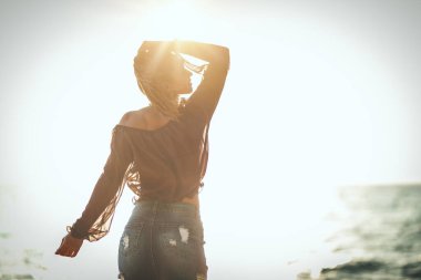 Güzel genç bir kadın sahilde dinleniyor. Poz veriyor ve gün batımına bakıyor..