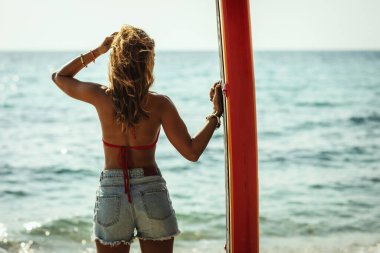 Deniz kıyısında sörf tahtası olan genç bir kadın dalgalar için hazır..