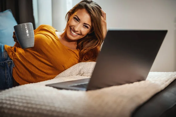 Atractiva Joven Bebiendo Café Tumbada Sofá Usando Portátil Para Navegar —  Fotos de Stock