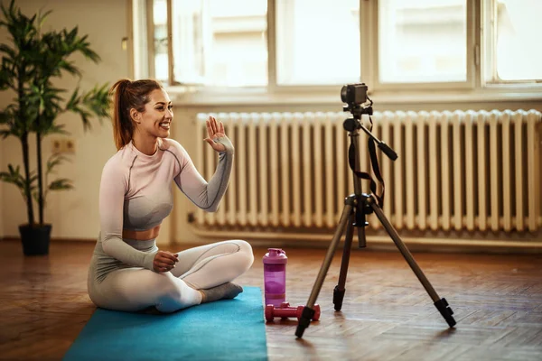 Young beautiful sporty woman vlogger is making video training for blog exercising in front of a home camera.