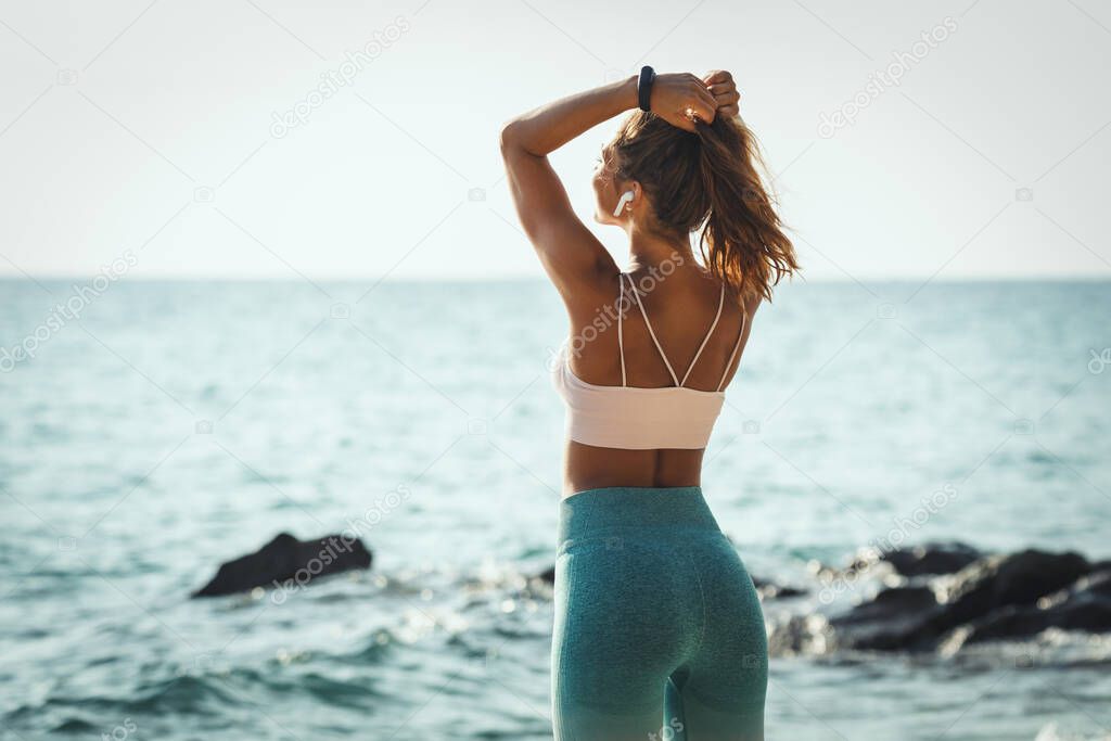 A beautiful young woman is doing stretching exercise at the sea beach in summer sunny day.