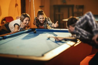 Genç gülümseyen neşeli arkadaşlar işten sonra barda bilardo oynuyorlar. Onlar eğlence aktivitelerine katılırlar..