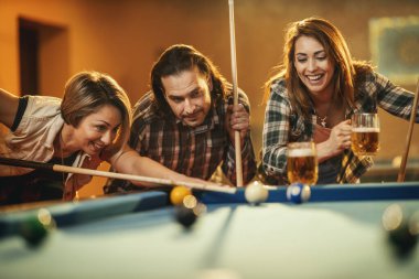 Genç gülümseyen neşeli arkadaşlar işten sonra barda bilardo oynuyorlar. Onlar eğlence aktivitelerine katılırlar..