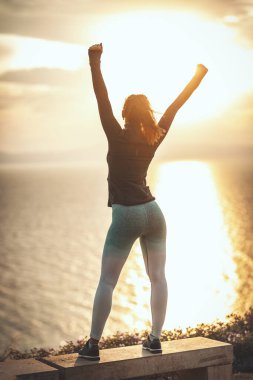 Güzel bir genç kadın gün batımında deniz sahilinde esneme egzersizi yapıyor..