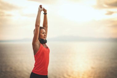 Güzel bir genç kadın gün doğumunda deniz sahilinde esneme egzersizi yapıyor..