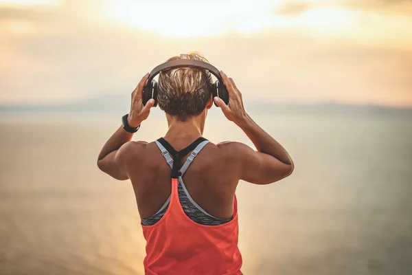 一位年轻貌美的女士准备在海边做伸展运动 在日出时听耳机里的音乐 — 图库照片