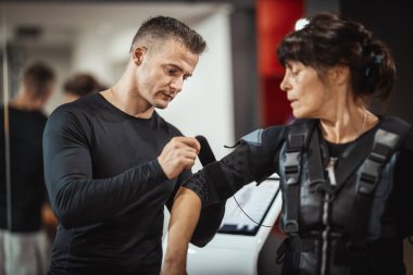 Kişisel antrenör, gülümseyen bir son sınıf kadınına sağlık ekibi için spor salonunda yardım ediyor..