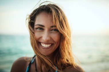 Güzel bir genç kadının portresi tropik sahilde poz veriyor ve eğleniyor. Kameraya bakıyorum..