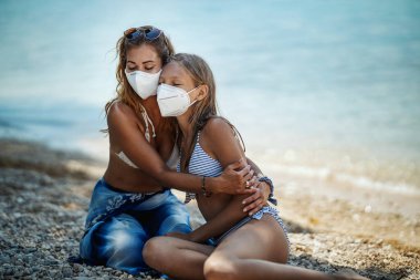 Korumalı N95 maskeli, gülümseyen bir kız kardeşin Corona Salgınında sahilde vakit geçirmesi. Doğada kendilerini izole ediyorlar..