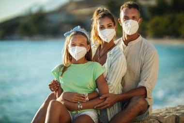 Korumacı N95 maskeli mutlu bir ailenin portresi Corona salgınında deniz kenarında vakit geçiriyor.. 