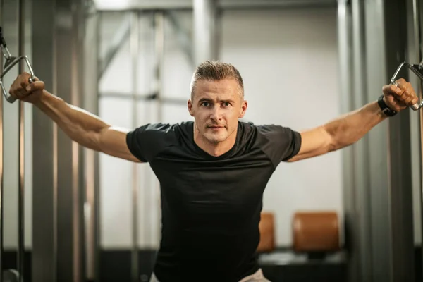 ジムでの筋力トレーニング中にケーブルマシンで胸のためのハード演習を行う筋肉の若い男 — ストック写真