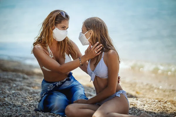 幸せな女の子と彼女の若いですお母さんとともに保護N95マスク過ごす時間でビーチにコロナパンデミック — ストック写真