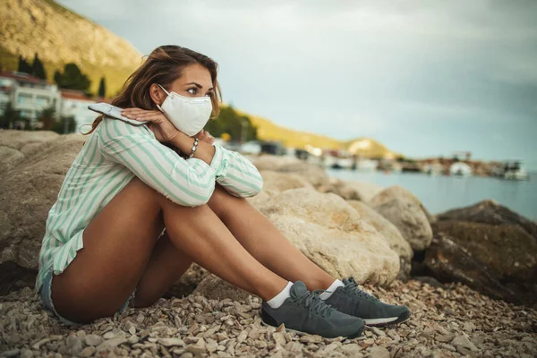保護N95マスクを持つ若い女性が座っているとCovid 19中にビーチで時間を過ごしながら心配しています — ストック写真