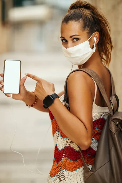拍摄快乐的年轻女子戴着保护面具 指着她的空智能手机屏幕在度假和探索地中海城市在日冕大流行 图库图片