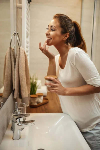 Tiro Uma Jovem Atraente Aplicando Creme Hidratante Facial Banheiro Casa — Fotografia de Stock