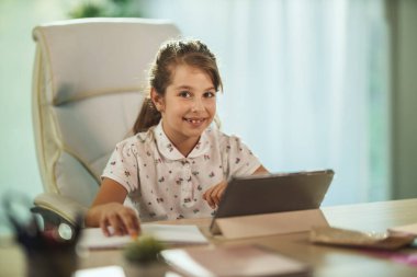 Çalışkan küçük bir kızın COVID-19 salgını sırasında evde online ders verirken tabletini kullanması..