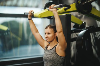Spor giyim bölümünde spor salonunda spor salonunda çalışan kaslı genç bir kadının fotoğrafı. O, omuz kaslarını ağır ağırlıkla şişiriyor..