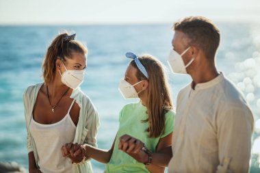 Korumacı N95 maskeli mutlu bir ailenin Corona salgınında deniz kenarında vakit geçirmesi. Doğada kendilerini izole ediyorlar..