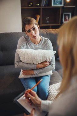 Stresli genç bir kadının kadın psikoterapistiyle oturma odasındaki bir kanepede otururken tartıştığı fotoğraf..