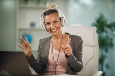 Çekici genç bir iş kadınının COVID-19 salgını sırasında evinde kulaklıklarla otururken ve dizüstü bilgisayarla çalışırken çekilmesi..