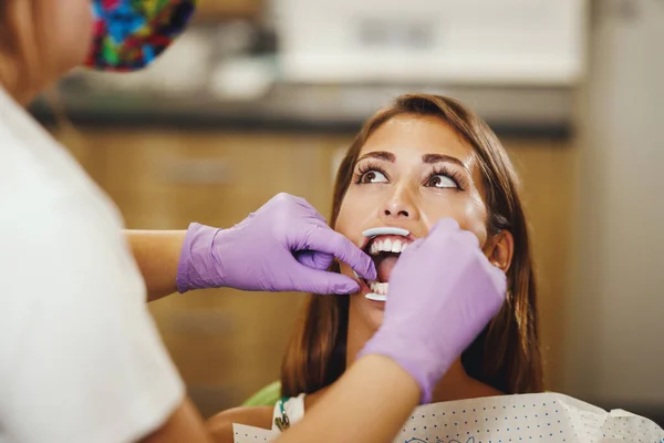 一个年轻貌美的女人在牙医那里被枪杀了 她坐在牙医的椅子上 牙医准备在她的牙齿上装上牙套 把美观的 自我调整的语言锁放在一起 — 图库照片
