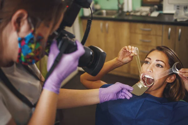 一个年轻貌美的女人在牙医那里被枪杀了 她坐在牙医的椅子上 牙医检查美观的 自我调整的语言锁 并在旁边拍照 — 图库照片