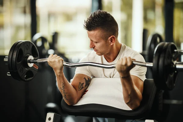 体育館でのハードトレーニングで働くスポーツウェアの筋肉の男のショット 彼は重い重量で二足の筋肉を汲み上げている — ストック写真