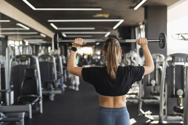 Back view of female doing shoulder workout with barbell. 