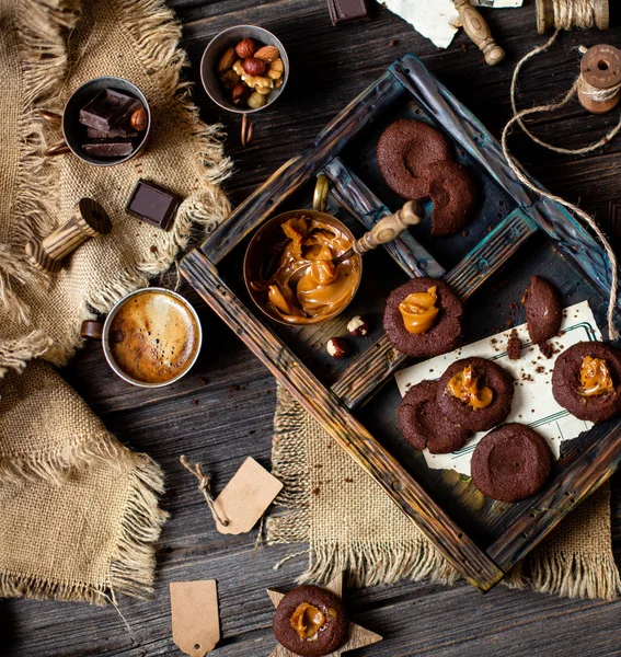 Overhead shot of homemade chocolate tasty cookies with caramel or condensed milk on dark blue wooden board with copper cup with caramel on rustic table