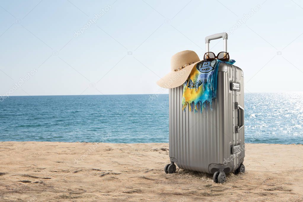 View of gray suitcase with pareo and hat on tropical  beach 
