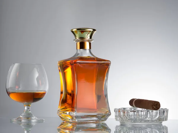 close up view of cigar, bottle of cognac and a glass aside on grey back.