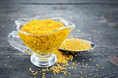 Bir kaşık ahşap tahta arka plan üzerinde cam sauceboat ve hardal tohumu hardal Dijon sos