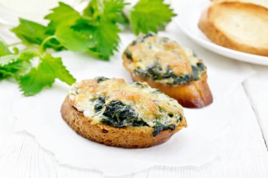 Isırgan otlu sıcak sandviçler ve buğday dilimli peynirli ekmek, parşömen üzerine parşömen, arka planda hafif ahşap tahtalar.