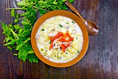 Soup from chicken meat, pasta with cream and sweet pepper, parsley and cilantro in a clay plate on the background of a dark wooden board on to