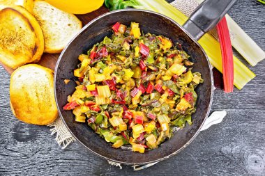 Çuval bezinde eski bir tavada portakal ve soğanlı sıcak pazı salatası, ekmek, çatal ve yukarıdan siyah ahşap bir arka plan.