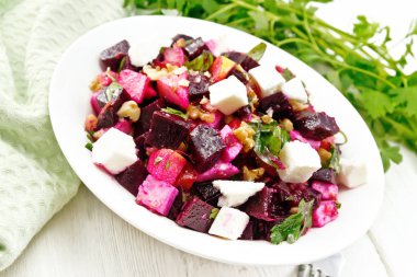 Pancar salatası, tuzlu peynir, elmalar, ceviz, maydanoz, balzamik sirke ve zeytinyağı ile tatlandırılmış bir tabak, ahşap bir arka planda yeşil peçete.