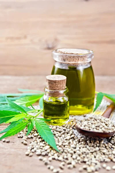 2つのガラス瓶に麻油 木の板の背景に大麻の葉や茎のナプキンに穀物のスプーン — ストック写真