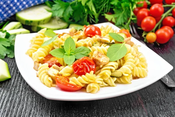 Fusilli with chicken and tomatoes in plate on black wooden board — Stock Photo, Image