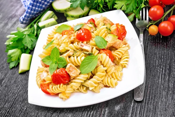 Fusilli with chicken and tomatoes in plate on dark board — Stock Photo, Image