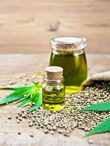 Oil hemp in two jars with grain on old board — Stock Photo, Image