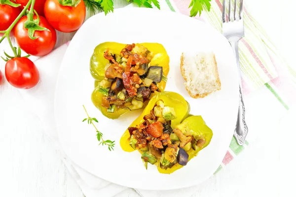 Перец фаршированный овощами в тарелке на легкой доске — стоковое фото