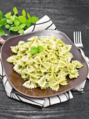 Pesto soslu Farfalle makarna, bir tabakta fesleğen, bir peçetede kara tahta karşı.