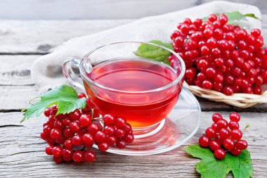 Cam bir fincanda viburnum, böğürtlenli hasır tabakta yeşil yapraklar ve eski bir tahta üzerinde çuval bezi olan çay.